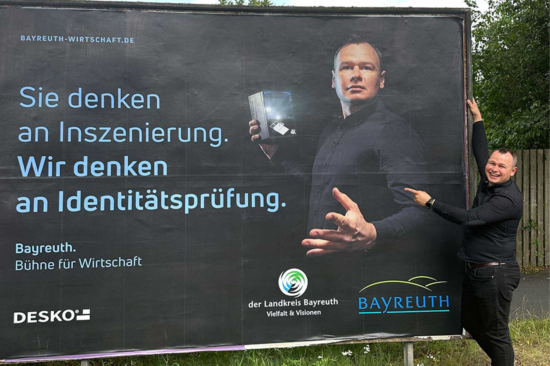 DESKO Mitarbeiter Wojciech Bujak steht vor einer Plakatwand, die ihn mit einem DESKO Scanner in der Hand zeigt.